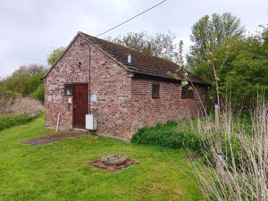 Photos of the old changing rooms showing its setting and the view from the entrance down Burns Playing Field. There are areas of mown grass with uncultivated natural vegetation to each side